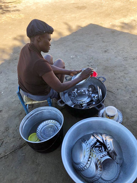 A cook at the school washes dishes using plastic totes outside