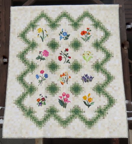 A quilt with a white background with a center of a green frame around colorful flowers.