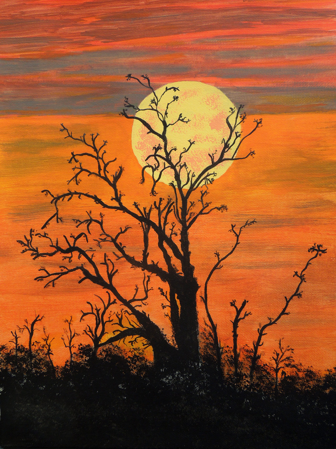 A yellow moon hangs in an orange and red sky with barren trees in front of it.