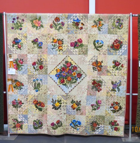 A colorful quilt with hand appliqués of colorful flowers on a muted pastel colored patchwork background.
