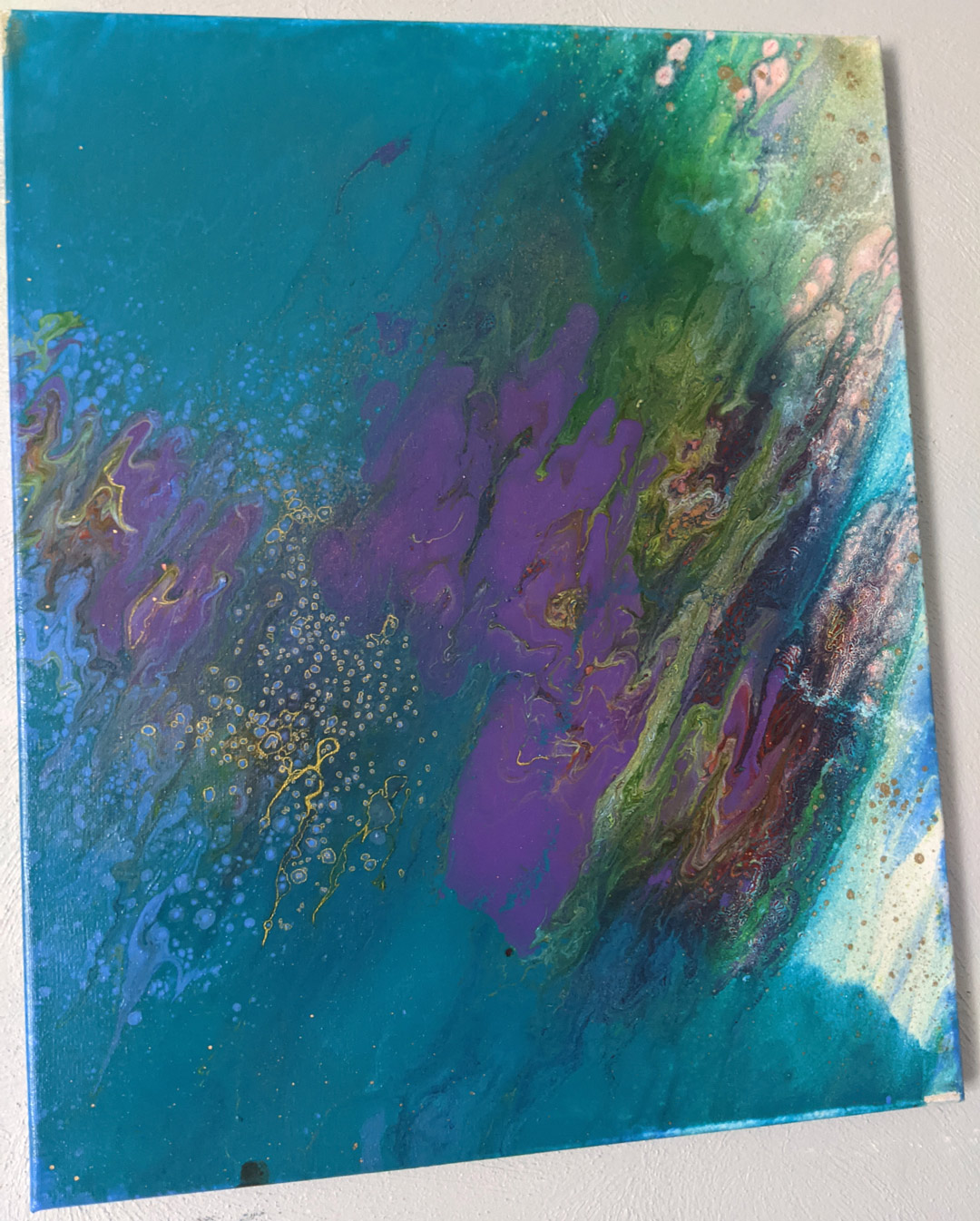 A tie-dye-like colorful painting of mostly teal with gold splatter. 