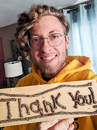 Logan holds up a hand-made wooden sign that says 'thank you'