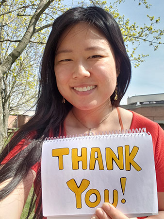 Cailee Ragonesi stands on campus and holds a thank you sign.