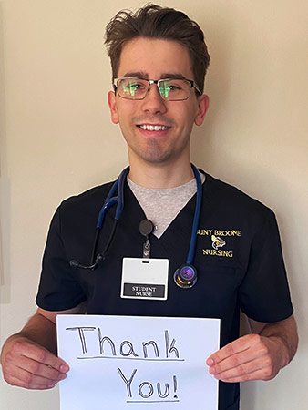 Gavin holds a thank you sign as he stands in his nursing scrubs.