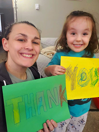 Harlee and her young daughter hold up crayon-written thank you signs.