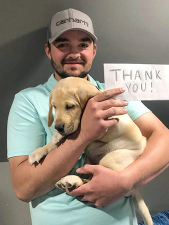 Nicholas holds a yellow lab puppy and a thank you note.