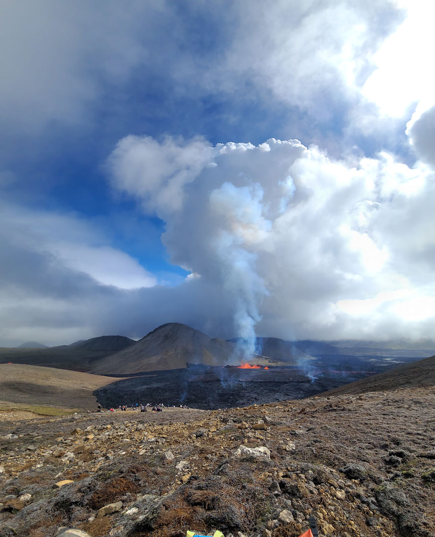 The Fagradalsfjall volcano with a plume of white smoke joining the clouds.