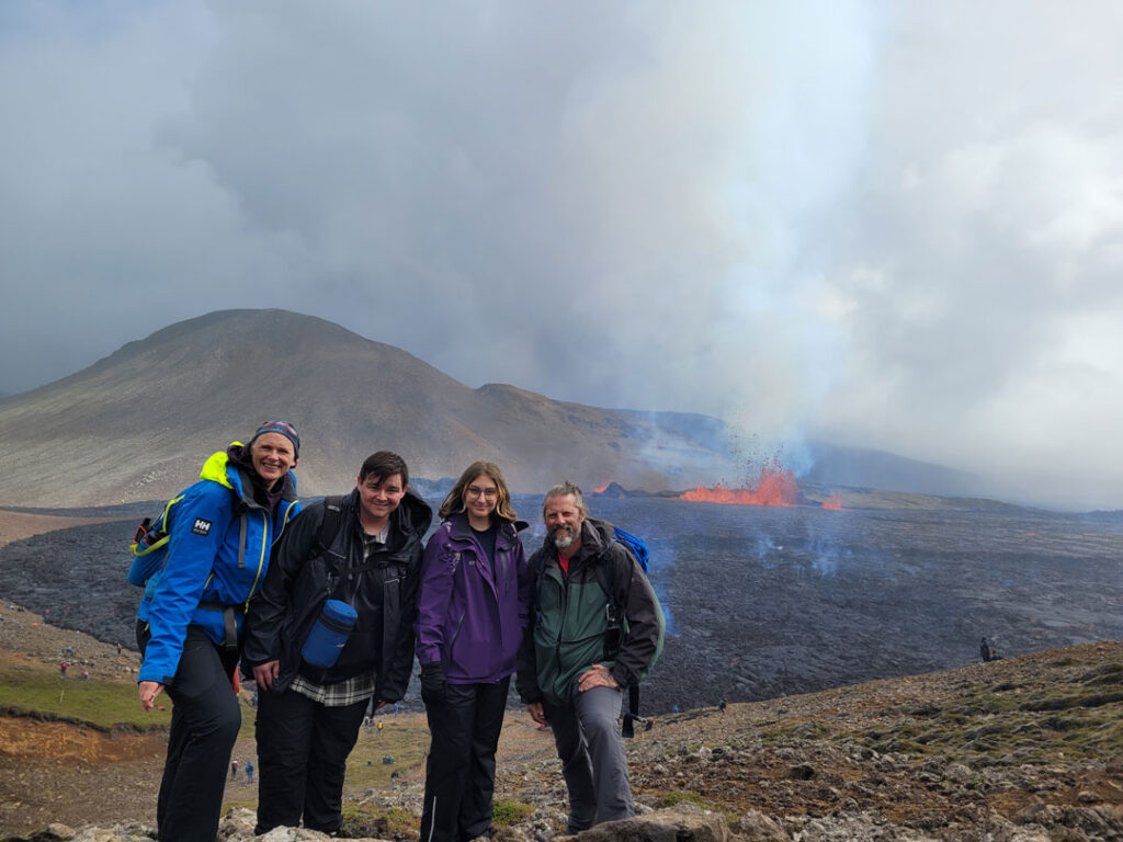 Two SUNY Broome professors and Students stand with the Fagradalsfjall volcano erupting behind them.