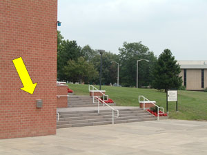 arrow pointing to blue light phone on the Decker Center on the Southeast corner (at base of stairs near Student Lot #1)